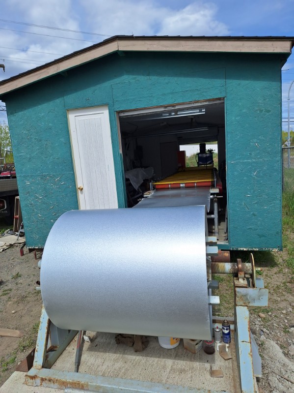 A picture showing the metal press with a long gray metal ready to be molded that lance chainlink uses to cut the Tuff-rib metal roofing panels in Prince-George.